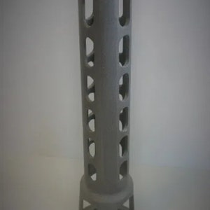 May include: A gray, cylindrical metal object with a flared top and base. The body features a series of rectangular cutouts. The object stands approximately 12 inches tall, with a circular base and a wider top.