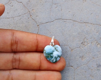 May include: A heart-shaped pendant made of moss agate with a silver bail. The stone is a light blue color with green moss-like inclusions.