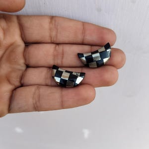 Pode incluir: Um par de brincos de meia lua com um padrão de tabuleiro de xadrez em preto e prata.