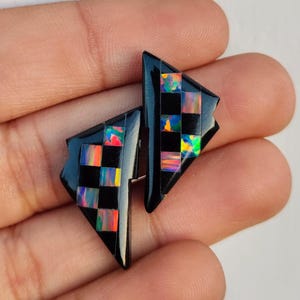 May include: A pair of black triangular earrings with iridescent checkerboard patterns.