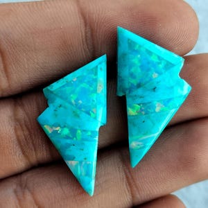May include: Two turquoise blue gemstone cabochons with a triangular shape and iridescent patterns.