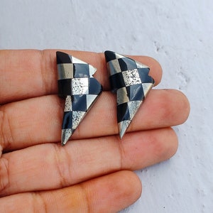May include: A pair of black and silver checkerboard patterned earrings. The earrings are shaped like a lightning bolt.
