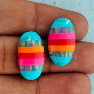 May include: Two oval-shaped turquoise cabochons with multi-colored inlay. The inlay features stripes of pink, red, orange, and iridescent blue.