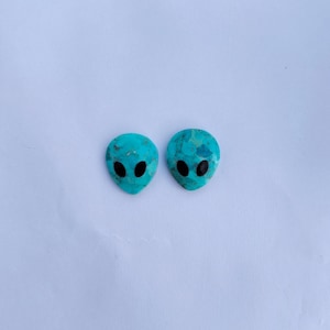 May include: Two turquoise blue alien head shaped cabochons with black eyes.