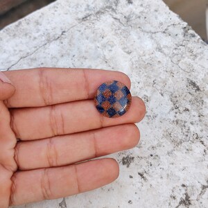 May include: A round, blue and brown checkerboard patterned button with a glittery finish.