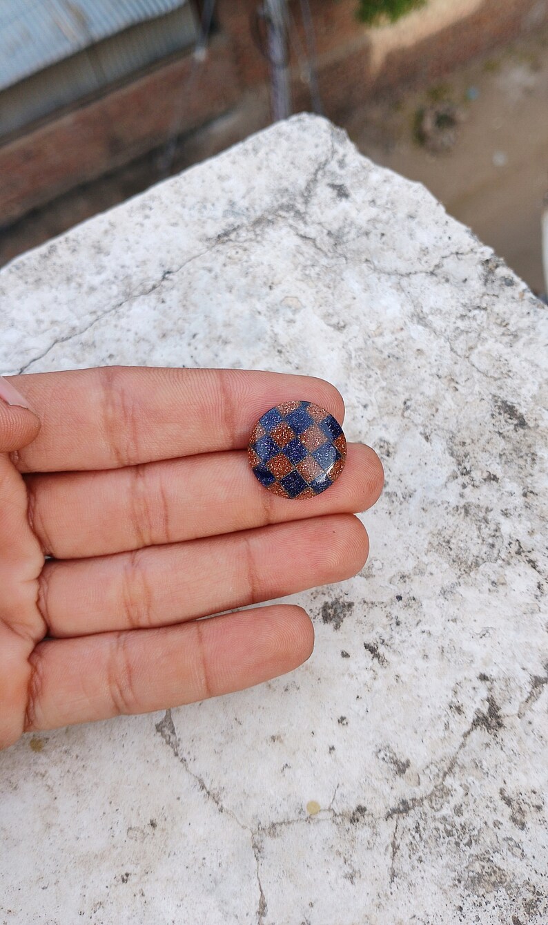 May include: A round, blue and brown checkerboard patterned button with a glittery finish.