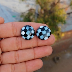 May include: A pair of round, black and white checkerboard patterned earrings. The earrings are made of mother of pearl.
