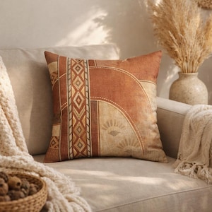 May include: A decorative throw pillow with a geometric pattern in shades of brown, tan, and cream. The pillow features a central vertical band with diamond shapes and a curved design on the right side. The pillow is placed on a beige sofa.