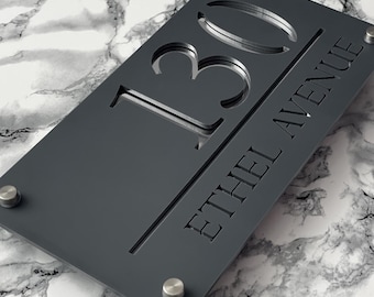 May include: A rectangular, dark gray address sign with the number "130" cut out, and the words "ETHEL AVENUE" etched below. The sign is mounted with four silver-colored screws on a marble-patterned surface.