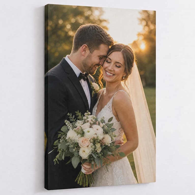 May include: A rectangular canvas print featuring a wedding portrait of a person in a black suit and a person in a white lace wedding dress with a veil, holding a bouquet of white and light pink flowers with greenery in a sunlit outdoor setting.