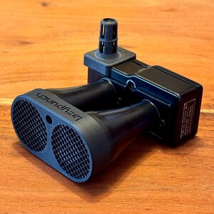 Op de afbeelding: Een zwarte tweetonige autohoorn met een zwarte kunststof luchtinlaatbuis. De hoorn heeft een zwarte kunststof behuizing met een zwart kunststof rooster aan de voorkant. De hoorn is aan de zijkant gemarkeerd met "soundizer".