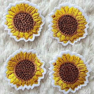 May include: Four embroidered sunflower patches with yellow petals and brown centers, each with a white border. The patches are arranged on a white, textured background, creating a cheerful and decorative design.