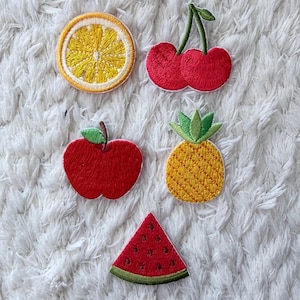 Könnte beinhalten: Gestickte Obstaufnäher, darunter eine Zitronenscheibe, Kirschen, ein roter Apfel, eine Ananas und eine Wassermelonenscheibe. Die bunten Aufnäher eignen sich ideal zum Aufnähen auf Kleidung oder Accessoires.
