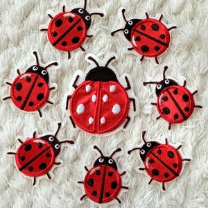 May include: A collection of seven embroidered ladybug patches. Six patches feature a red body with black spots and a black head, while one larger central patch features a red body with white spots and a black head. Each patch has a white border.