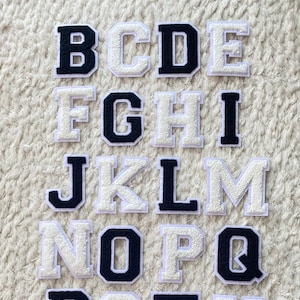 May include: A collection of fabric letter patches in a variety of fonts. The letters are in a navy blue and white color scheme. The letters are arranged on a white, textured surface.