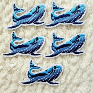 Könnte beinhalten: Fünf gestickte Wal-Patches. Jeder Patch zeigt ein blaues Wal-Design mit verschiedenen Blau- und Weißtönen. Die Wale sind vor einem weißen Hintergrund platziert.