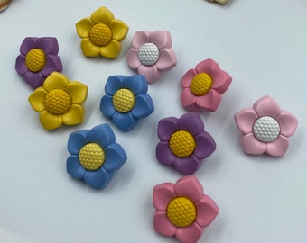 May include: Assortment of colorful flower-shaped buttons in shades of yellow, pink, blue, and purple. The buttons have a raised center and a textured surface.