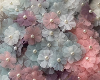 May include: A collection of pastel-colored fabric flowers with pearl centers. The flowers are arranged in a random pattern and are all different sizes.