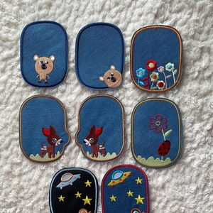 Peut inclure: Neuf patchs brodés thermocollants avec différents motifs. Les patchs sont bleus avec des accents orange, rouge, jaune et blanc. Les motifs comprennent un ours, un cerf, une fleur, une coccinelle et un astronaute.
