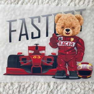 Pode incluir: Um carro de corrida vermelho com o número 83 no lado, um urso de peluche vestindo um macacão de corrida vermelho com a palavra "RACER" no peito e a palavra "FAST" em letras pretas.