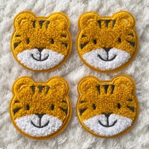 Może przedstawiać: Cztery żółto-brązowe, puszyste łatki z twarzami tygrysa z białymi uśmiechającymi się ustami i czarnymi oczami.