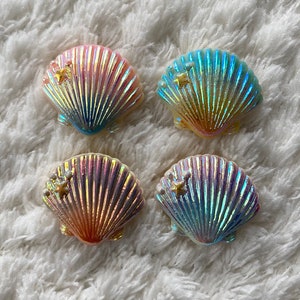 Könnte beinhalten: Vier regenbogenfarbene Muschel-förmige Harz-Anhänger mit einem goldenen Stern-Akzent. Die Muscheln sind in den Farben Rosa, Blau und Grün.