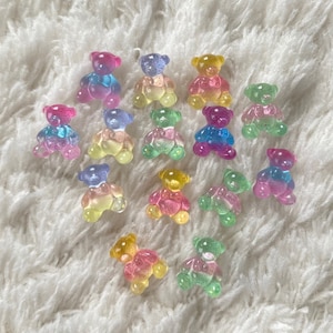 Puede incluir: Una colección de 15 pequeños amuletos con forma de osito de goma, de colores vivos. Los amuletos son translúcidos y tienen un efecto degradado arcoíris.