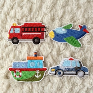Op de afbeelding: Vier geborduurde patches met transportvoertuigen. Inclusief een rode brandweerwagen, een blauw vliegtuig met groene vleugels, een groene en blauwe boot en een blauwe politieauto met het woord "POLICE".
