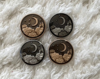 May include: Four round metal buttons with a crescent moon and stars design. The buttons are in two different color combinations: silver with a black moon and gold with a brown moon.