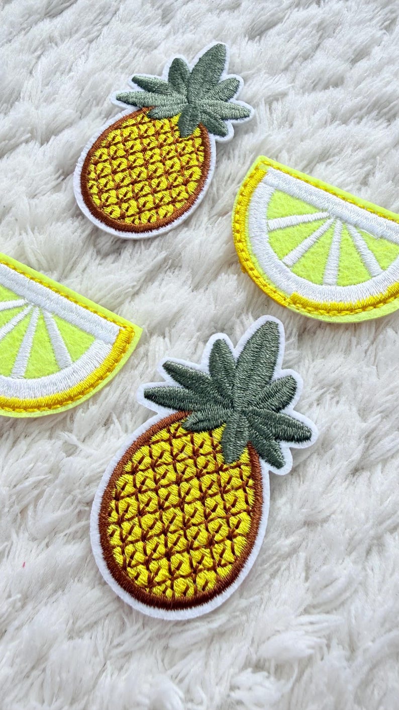 May include: Embroidered patches of a pineapple and lemon slices. The pineapple patches have a yellow body with brown outlines and green leaves. The lemon slices are yellow with white outlines. These patches are ideal for adding a touch of summer to clothing or accessories.