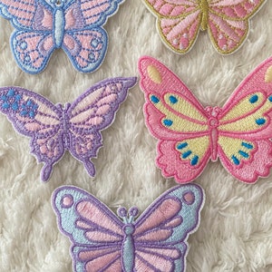 May include: Five embroidered butterfly patches in various pastel colours, including pink, purple, blue, and yellow. The butterflies are all different sizes and have intricate details.