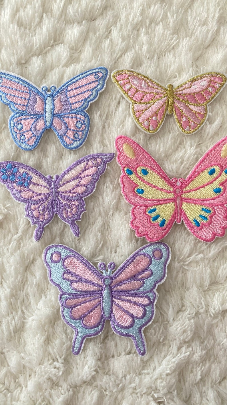May include: Five embroidered butterfly patches in various pastel colours, including pink, purple, blue, and yellow. The butterflies are all different sizes and have intricate details.