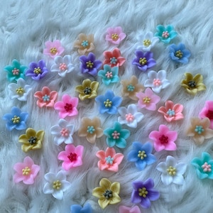 Könnte beinhalten: Eine Sammlung von pastellfarbenen Blumenverzierungen, perfekt, um Ihren Bastelarbeiten und Projekten einen Hauch von Verspieltheit zu verleihen. Die Blumen sind aus einem weichen, biegsamen Material gefertigt und in verschiedenen Formen und Größen erhältlich.