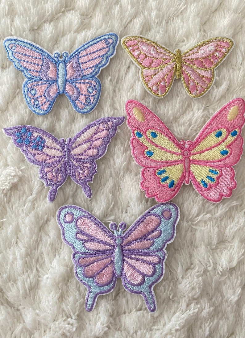 May include: Five embroidered butterfly patches in various pastel colours, including pink, purple, blue, and yellow. The butterflies are all different sizes and have intricate details.