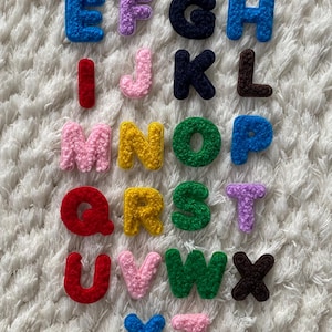 Puede incluir: Un conjunto de 26 letras de fieltro de colores, cada letra es de un color diferente y tiene una textura peluda. Las letras están ordenadas alfabéticamente.