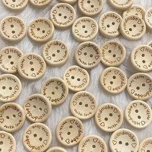 Puede incluir: Una colección de botones redondos de madera con el texto "Handmade with love" grabado en ellos. Los botones son de color marrón claro y tienen dos agujeros cada uno.