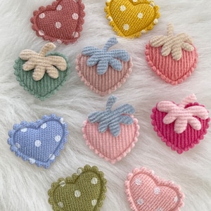 May include: Nine felt heart-shaped patches with white polka dots and a green, blue, or pink felt leaf on top. The patches are in various colors, including pink, red, blue, green, and yellow.
