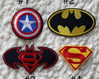 May include: Four iron-on patches featuring superhero logos.  #1 is a red, white, and blue Captain America shield. #2 is a black and yellow Batman logo. #3 is a black Batman logo with a red Superman logo inside. #4 is a yellow Superman logo.