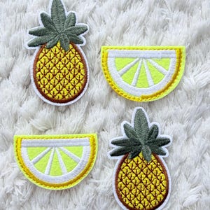 May include: Four embroidered patches with tropical fruit designs. Two pineapple patches with yellow and brown details and green leaves. Two lemon slice patches with yellow and white details. All patches have a white border and are on a white, textured background.