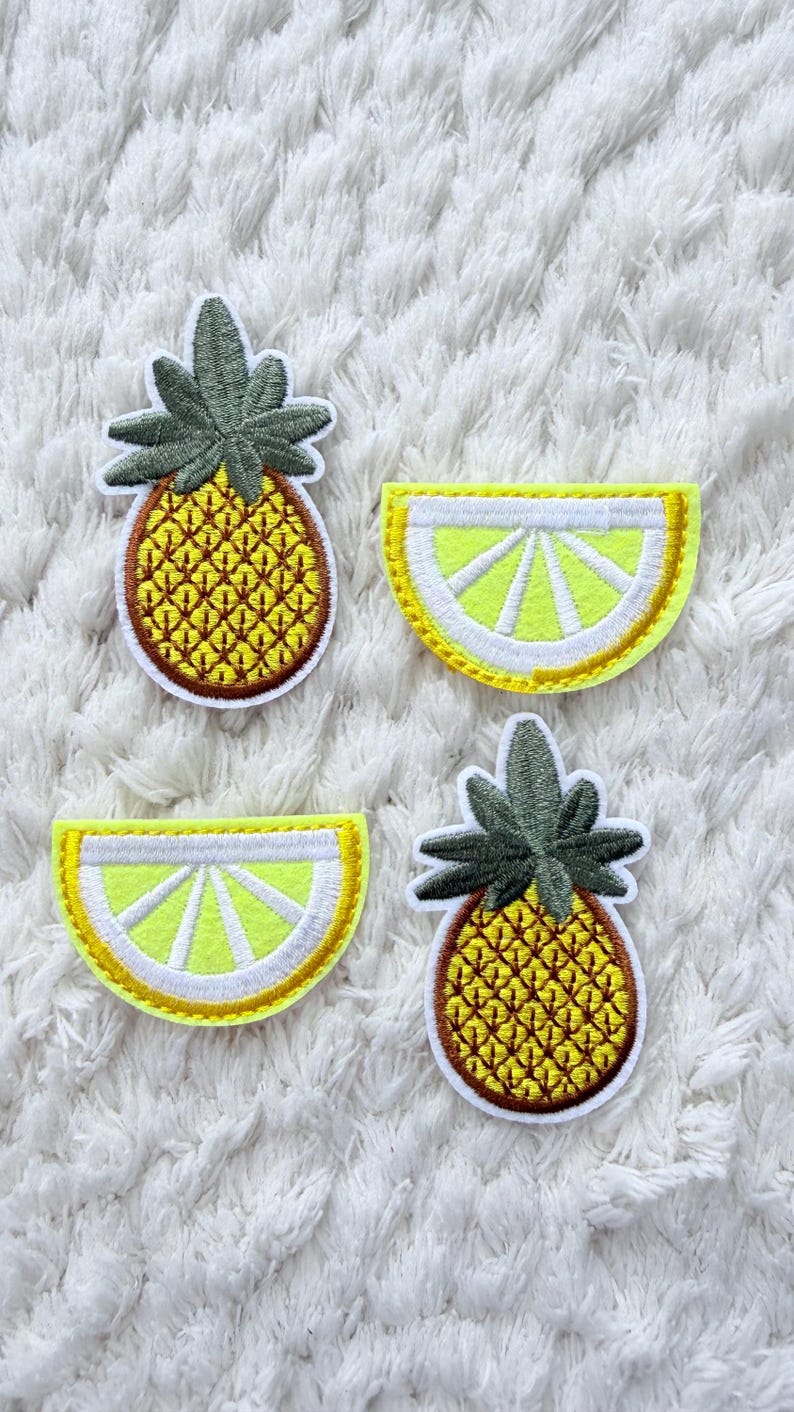 May include: Four embroidered patches with tropical fruit designs. Two pineapple patches with yellow and brown details and green leaves. Two lemon slice patches with yellow and white details. All patches have a white border and are on a white, textured background.