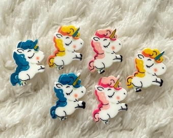 May include: Six colorful unicorn figurines with closed eyes and gold horns. The unicorns are in various colors, including blue, pink, yellow, and white.