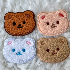 Könnte beinhalten: Vier flauschige, bärenförmige Patches in Braun, Rosa, Weiß und Beige. Die Patches sind mit Gesichtszügen bestickt und eignen sich perfekt, um Kleidung, Taschen oder anderen Accessoires eine süße Note zu verleihen.