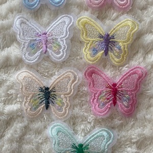 May include: Six embroidered butterfly patches in various colors, including blue, pink, yellow, white, and green. The butterflies are all on a white fluffy background.