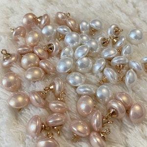 Op de afbeelding: Een verzameling witte en roze parels met gouden accenten. De parels zijn willekeurig gerangschikt op een wit, pluche oppervlak.