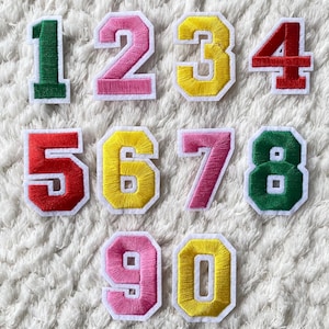 Puede incluir: Diez parches de fieltro de colores en forma de números del 1 al 10 para planchar. Los números están delineados en blanco y tienen un estilo vintage.