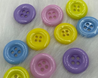 May include: Assortment of colorful plastic buttons with four holes each. The buttons are in shades of yellow, blue, purple, and pink.