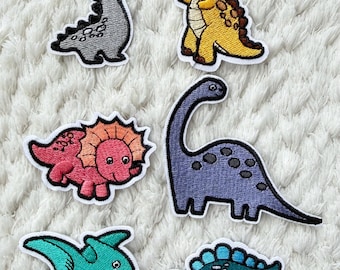 May include: Embroidered dinosaur patches in various colors, including gray, yellow, pink, purple, teal, and blue. Each patch features a different dinosaur design with a white border. These patches are ideal for adding to clothing or accessories.