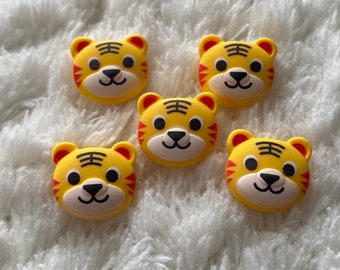 May include: Five yellow tiger face buttons with black stripes and red accents. The buttons are on a white fluffy surface.