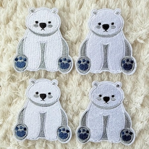 May include: Four white polar bear patches with gray accents and dark blue paw pads are arranged on a white, textured surface. Each patch features a black nose and small eyes, creating a cute, cartoonish design.
