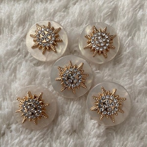 May include: Five white round buttons with gold starburst designs and clear rhinestones.